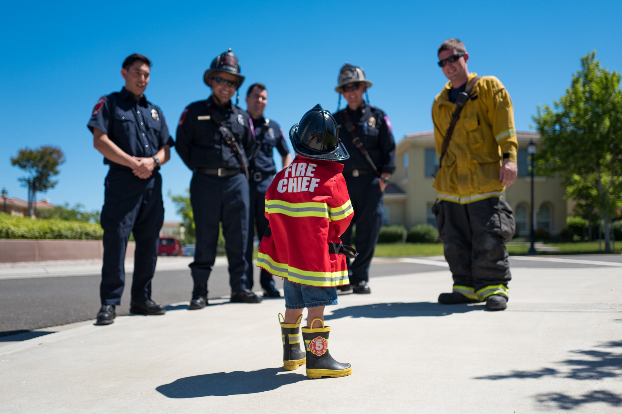 child in a firefighter's outfit standing facing a group of firefighters